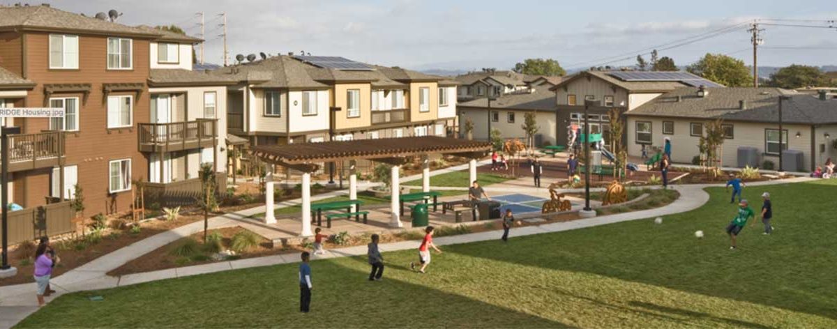 sunny, grassy multifamily affordable housing complex with large playground, children playing, multiple generations