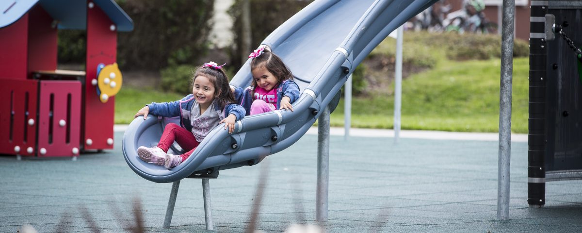 Two kids going down a slide at a park.
