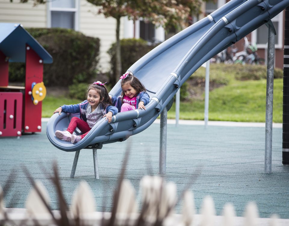 Two kids going down a slide at a park.
