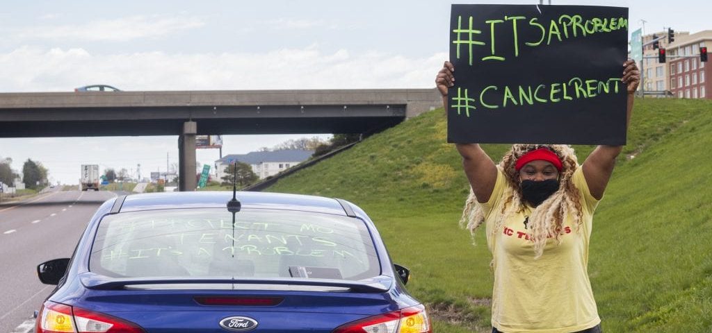 image of woman holding a rent strike sign on the side of the road.