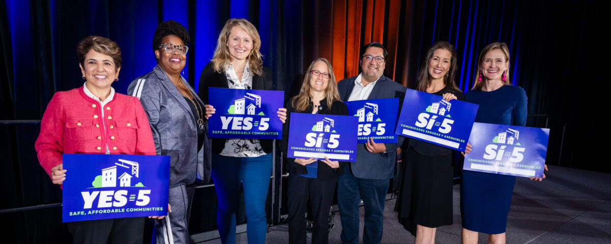 Panel of Conference speakers holding prop 5 signs