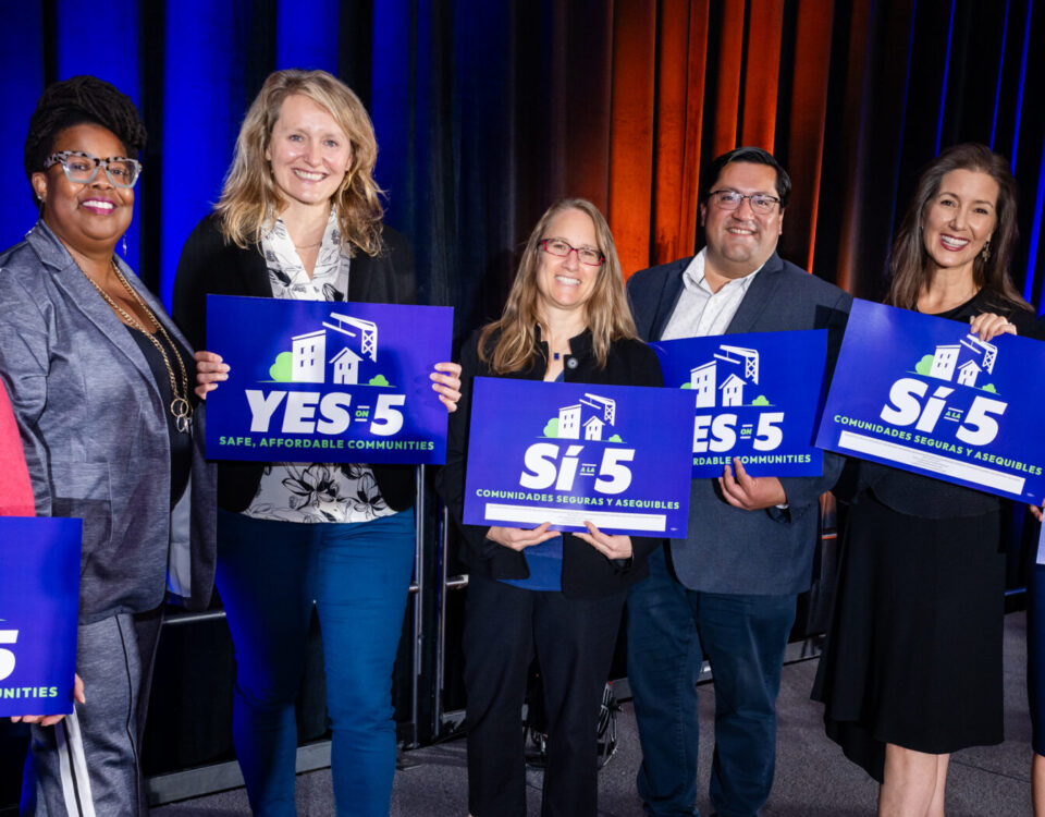 Panel of Conference speakers holding prop 5 signs