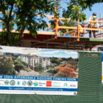 Green fence with sign that signifies affordable housing is being built. Workers in the background out of focus